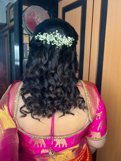 A back view of this half-up hairstyle. The curls are soft and bouncy, and the line of baby's breath adds a beautiful decorative element.