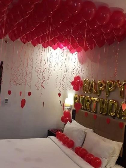 A simple and elegant romantic room setup with red balloons covering the ceiling and 'Happy Birthday' foil letters above the bed.