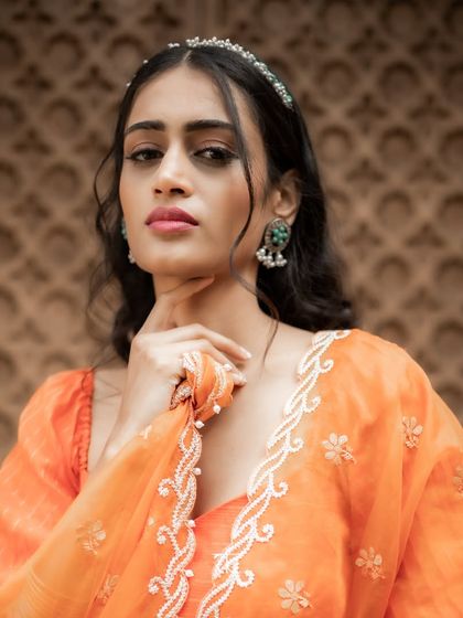 A portrait highlighting the delicate thread and pearl embroidery on the border of the orange organza dupatta.