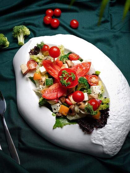 A fresh, colorful salad served in a unique, artistic white bowl. The lighting is bright and clean, emphasizing the freshness of the ingredients.
