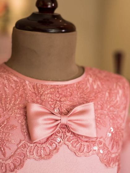 A close-up of the exquisite lace and sequin detailing on this pink bodice. The scalloped edge of the lace creates a beautiful neckline, topped with a simple satin bow.