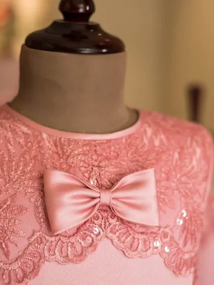 A close-up of the exquisite lace and sequin detailing on this pink bodice. The scalloped edge of the lace creates a beautiful neckline, topped with a simple satin bow.