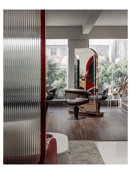 A fluted glass partition with a deep red frame separates spaces while allowing light to pass through. This detail shot shows the styling area beyond, highlighting the mix of textures and materials used throughout the salon.