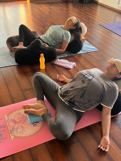 Students relax in Supta Baddha Konasana (Reclined Bound Angle Pose) supported by bolsters. This restorative pose is excellent for opening the hips and calming the nervous system.