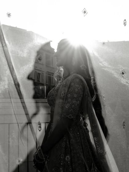 An artistic black and white shot of the bride's silhouette against the sun. The light shining through her veil creates a beautiful, ethereal effect.