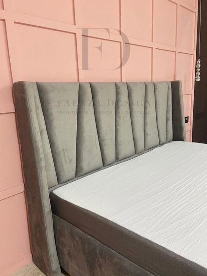 A modern and stylish bed with a winged, vertically-tufted headboard in grey velvet. Set against a pink paneled wall, this design shows how we use color and texture to create unique, personalized spaces.