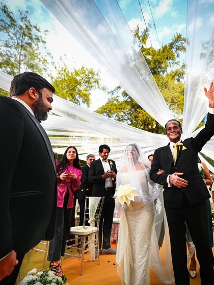 A proud father waves to guests as he walks his daughter down the aisle. Using a wide lens captures the joy of the moment and the beauty of the outdoor ceremony.