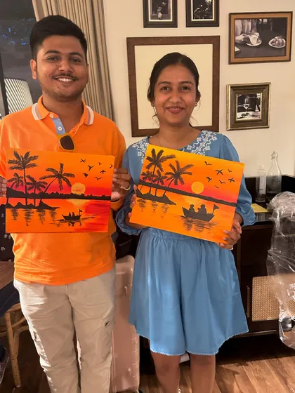 A happy couple posing with their matching sunset silhouette paintings.