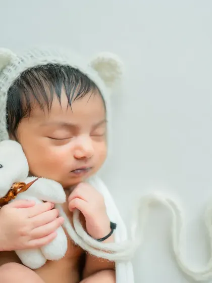 A simple and pure portrait with a white-on-white theme. The adorable bear bonnet and tiny teddy bear add a touch of sweetness.