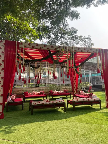 A vibrant red and white canopy for an outdoor ceremony. This traditional 'shamiana' style setup, complete with low seating and bolsters, is perfect for a relaxed and festive pre-wedding event.