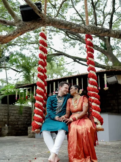 A cross-cultural couple enjoys a moment on the swing, decorated with red and white flowers, a vibrant and happy scene.