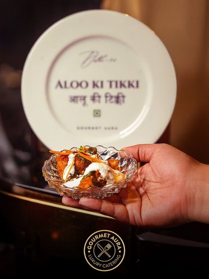 A guest holds a small bowl of our Aloo Ki Tikki chaat, served from a station with a custom-branded plate. We blend interactive service with personalized branding.