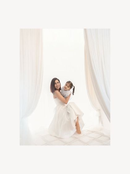 The warmth of color brings a different feeling to this moment of a mother and daughter's embrace. Their smiles radiate pure joy in the clean, white studio setting.