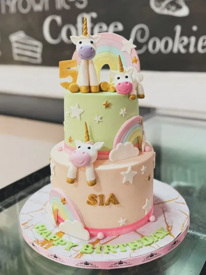 A two-tiered unicorn cake in pastel green and pink. This magical design is decorated with fondant unicorns, rainbows, and stars for a whimsical celebration.