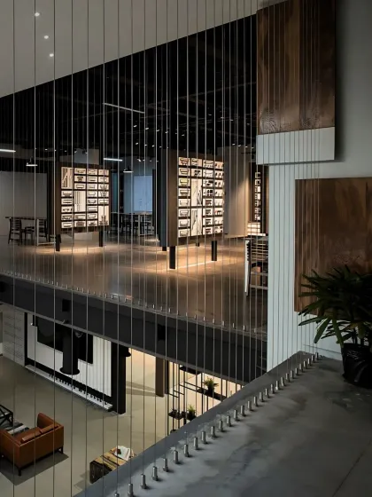 A view from the mezzanine level of a showroom, highlighting the use of vertical space and industrial materials like steel cables for railings. The design creates an open, multi-layered experience for visitors.