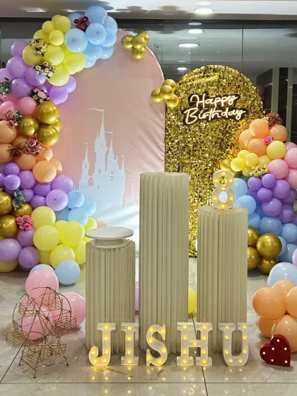 A magical castle-themed birthday party. The setup features a pastel balloon arch, a shimmering gold sequin backdrop panel, and light-up marquee letters, perfect for a princess celebration.