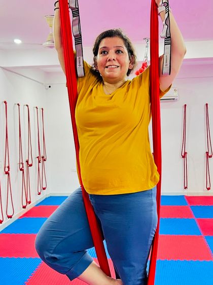 The joy of aerial yoga is accessible to everyone. This student smiles as she enjoys a moment of rest and balance in a supported tree pose.