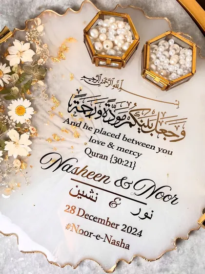 This elegant white and gold resin tray is perfect for a classic and timeless wedding theme. It features beautiful branch-style handles, delicate daisy accents, and is personalized with the couple's names and a Quranic verse in stunning calligraphy.