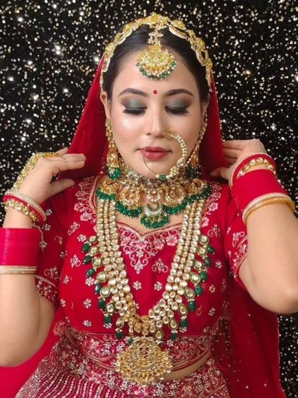 A bride wearing a full red lehenga and a heavy Kundan and emerald jewellery set. The long rani haar adds an extra layer of grandeur.