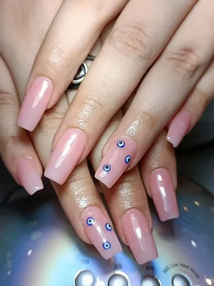 A simple yet trendy set of long, pink-toned acrylic nails with small "evil eye" decals.