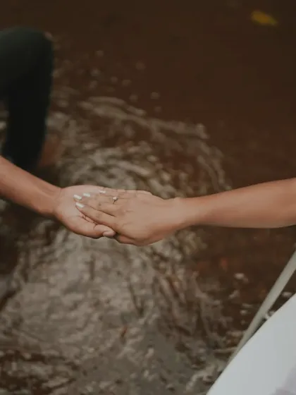 An artistic and symbolic shot of a couple holding hands while seated in chairs surrounded by water. This conceptual photo is about connection and trust.