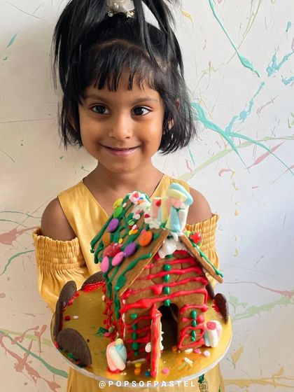 A little girl is thrilled with her candy-covered gingerbread house, a sweet treat she made herself.