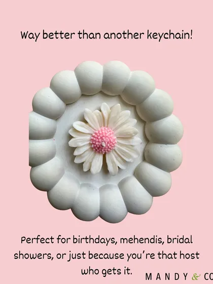 A pink daisy candle presented as a far better alternative to a generic keychain, perfect for a host with great taste.