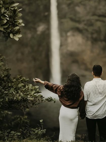A couple with their arms outstretched, embracing the beauty of the waterfall and the moment, seen from behind.