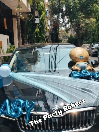 Another car decoration for a baby's arrival, with a blue net sash and "BABY BOY" foil balloons on the hood.