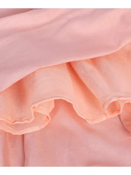 A close-up of the ruffled hem and double-layered fabric of a pink baby dress.