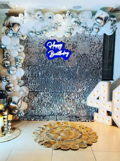 A glamorous 40th birthday photo booth with a silver sequin wall, a blue neon sign, and silver and white balloon decor.