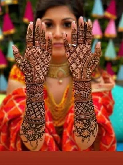 A bride frames her face with her hands, showing off a classic and intricate check-patterned mehendi design.