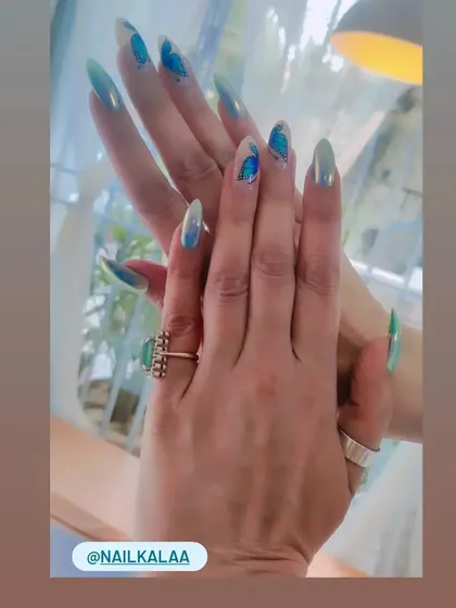 A gorgeous set of long stiletto nails with a green and blue shifting chrome finish. The abstract blue art on top adds another layer of detail.