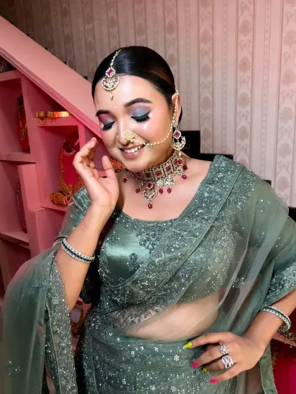 A student's work on a model, creating a soft glam look with a beautiful sage green lehenga. This is a popular style for receptions and sangeets.