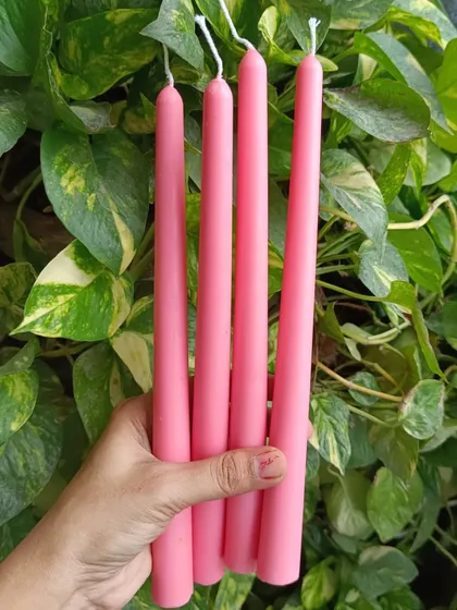 A set of four pink taper candles, hand-held to show their length and color.