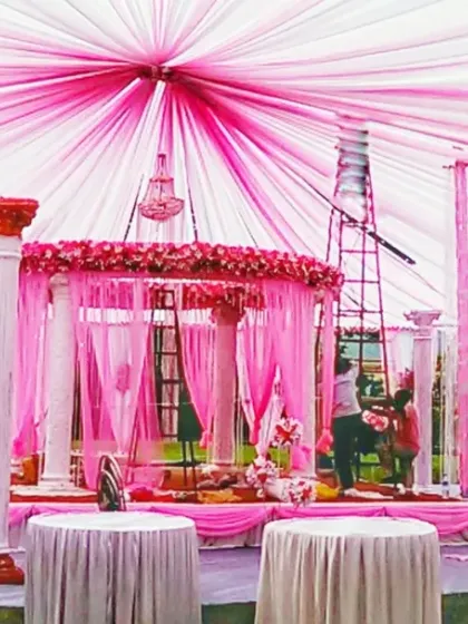 A large-scale pandal construction in progress, showing the pink fabric ceiling and pillar setup for a grand wedding mandap.