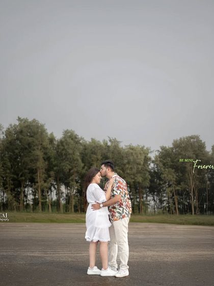A tender forehead kiss against a backdrop of trees and an open sky. This is a classic romantic pose that feels timeless and full of affection, perfect for any couple's photoshoot.