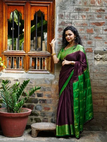 A beautiful portrait of a woman in a traditional saree, posing gracefully next to a classic wooden window.