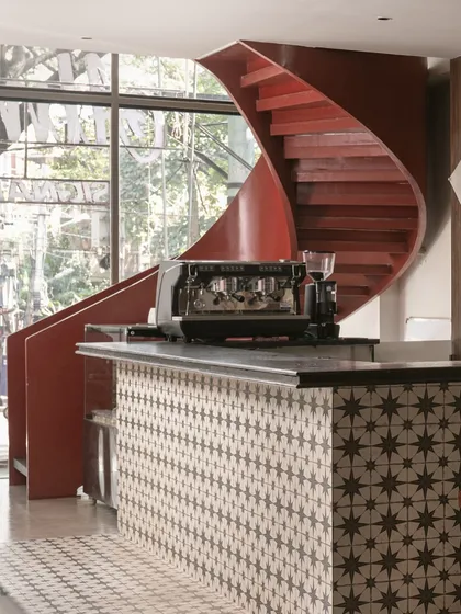The vibrant red spiral staircase serves as a stunning backdrop to the coffee bar. Its bold form contrasts with the patterned tiles and industrial-style counter, creating a focal point that is both functional and artistic.