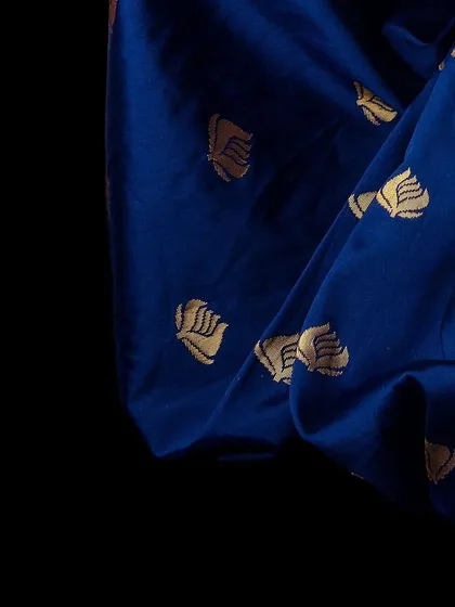 An abstract, artistic shot focusing solely on the rich blue fabric and golden motifs of the saree. This image serves as a beautiful texture shot for a lookbook, emphasizing the quality and design of the material itself.