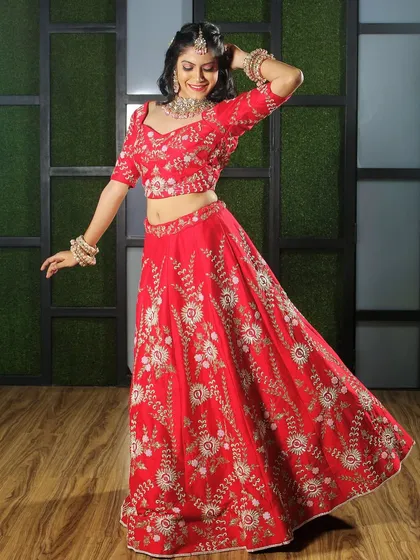 A playful, dynamic pose in the studio to showcase how the lehenga moves. This shot is great for social media content, showing the outfit in a fun and engaging way while still highlighting the detailed floral embroidery on the red fabric.