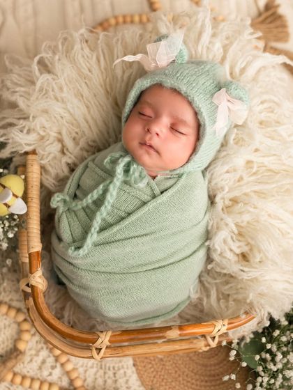 This newborn is swaddled in a soft mint green wrap and nestled in a basket with a fuzzy blanket. The little bee prop adds a sweet, whimsical touch.