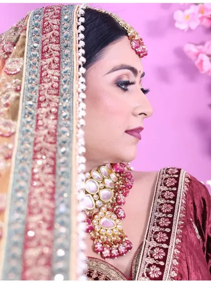 A side profile of a bride in a deep maroon velvet lehenga, showcasing the detailed embroidery on the dupatta and blouse. The look is completed with a heavy polki necklace set.
