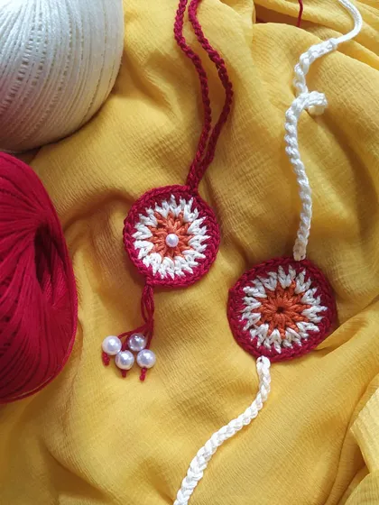 A beautiful Rakhi and Lumba set displayed with loose yarn, showing the raw materials of our craft. This set features a floral design with delicate pearl tassels.