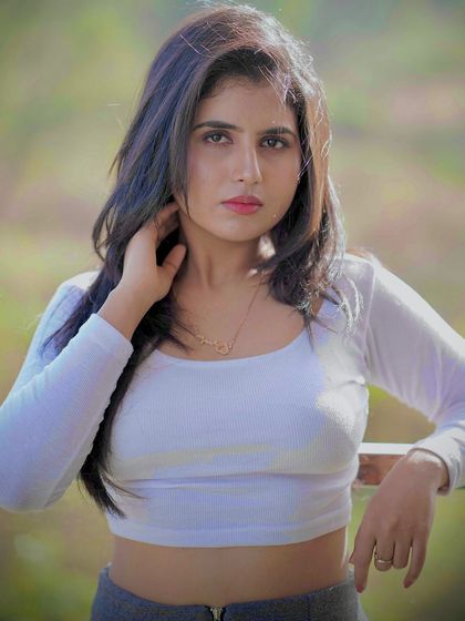 A confident pose in a casual outfit, taken outdoors with a natural, bright light.