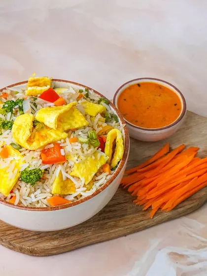 An egg and vegetable fried rice bowl, garnished with fresh parsley and served with a side of sauce. This image is shot with a clean setup to highlight a classic comfort food option for any menu.