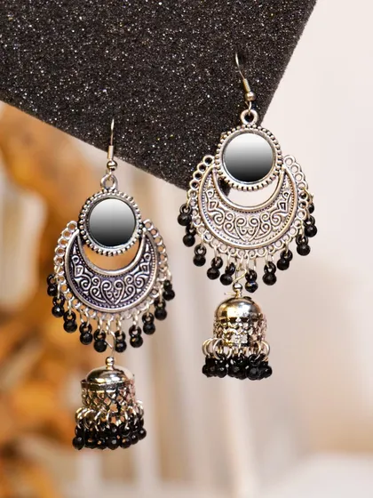 A close-up of silver and black ethnic jhumka earrings with mirror work. This detailed shot showcases the traditional craftsmanship and design elements.