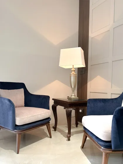 We believe in creating visual balance through contrast. Here, two custom armchairs upholstered in deep blue velvet provide a rich counterpoint to the neutral wall paneling, while their clean, mid-century lines maintain a modern sensibility.
