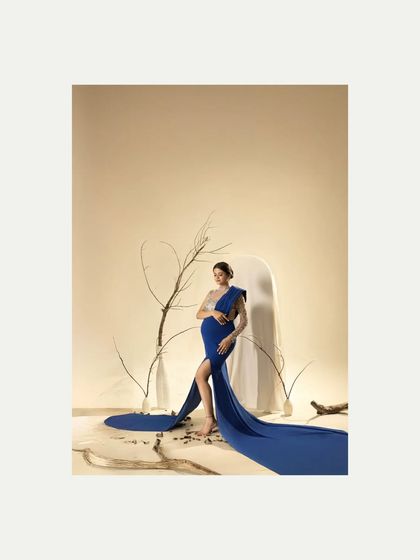 A wide shot of the dramatic blue gown, showing the full effect of the flowing fabric against the minimalist studio background. This composition emphasizes the fashion-forward styling of the shoot.