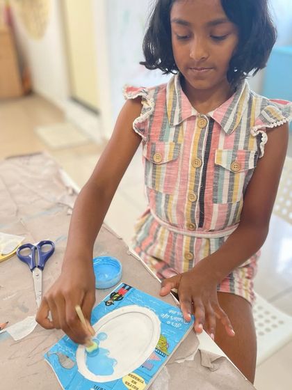 A young girl learns the art of decoupage, applying decorative paper to a photo frame.